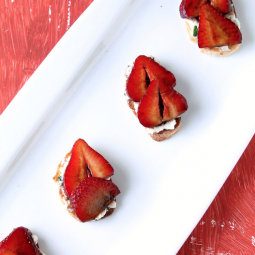 Crostini topped with goat cheese and sliced strawberries arranged on a white serving platter.