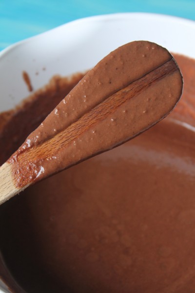 Wooden spoon covered in a chocolate ice cream base mixture, with a straight line running through the middle where a finger has swiped a line across the spoon.