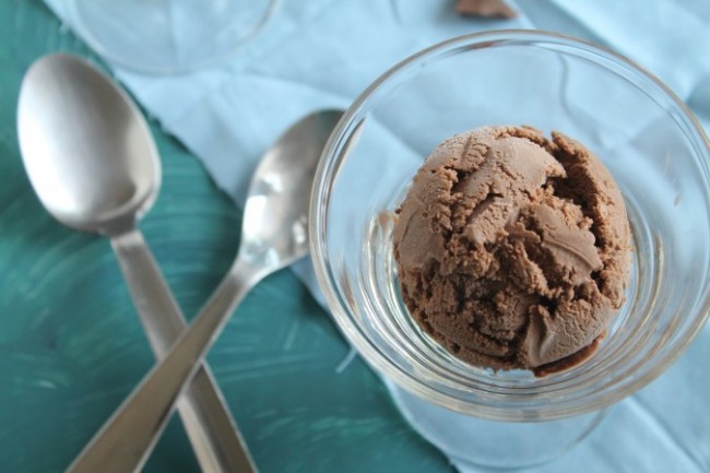 A scoop of chocolate ice cream in a glass serving dish next to two spoons.