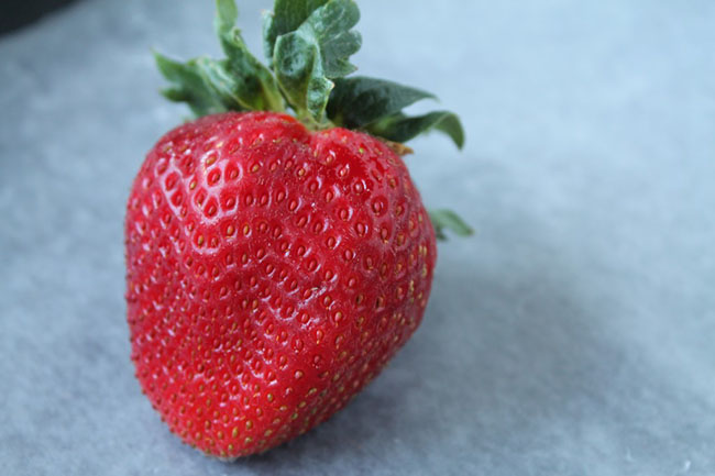 A fresh strawberry sitting on a baking sheet lined with parchment paper.