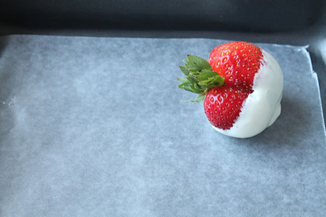 Fresh strawberry dipped in white chocolate sitting on a baking sheet.