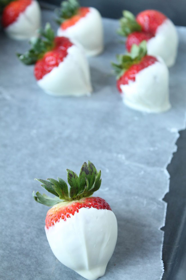 Seven fresh strawberries dipped in white chocolate and sitting on a baking sheet.