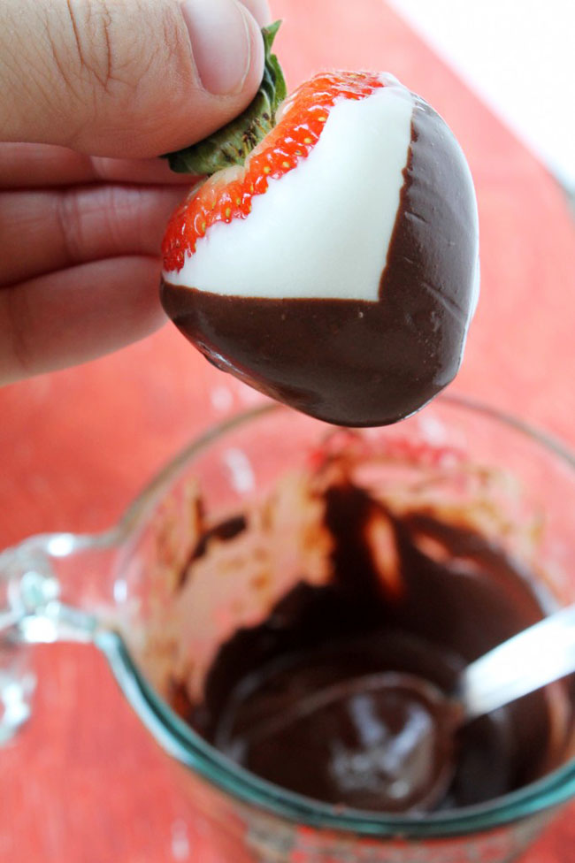 Woman\'s hand dipping a strawberry into a bowl of melted dark chocolate.