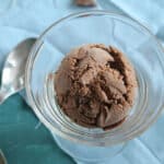 Tall glass serving dish filled with a scoop of chocolate ice cream on a blue table.
