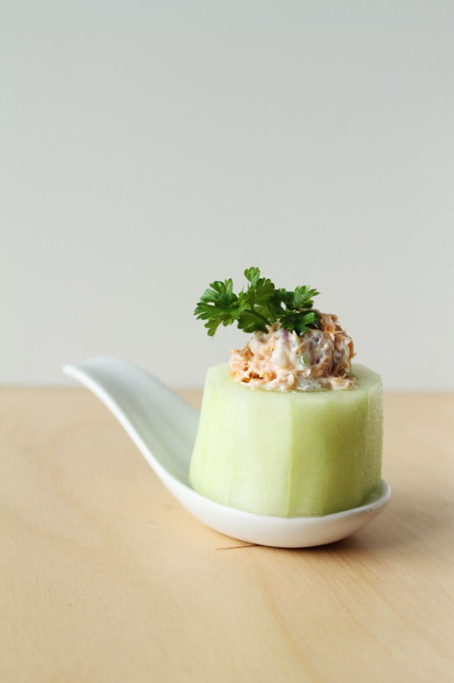 Cucumber cup stuffed with smoked salmon dip on a white appetizer spoon.