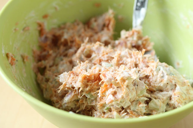 Silver spoon stirring smoked salmon dip together in a small green bowl.
