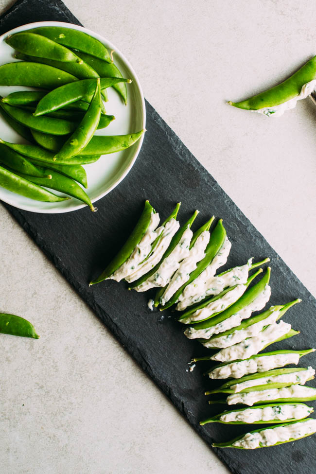 Stuffed snap peas arranged on a slate serving platter, next to a small plate of fresh whole snap peas.