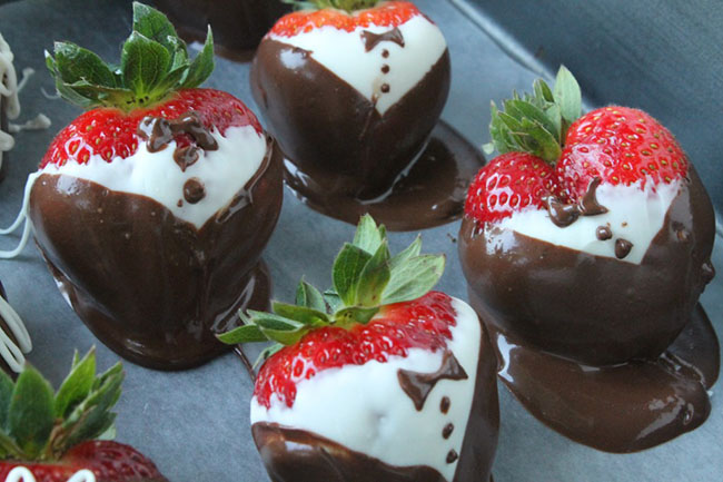 Chocolate covered strawberries with chocolate bow ties on a baking sheet lined with parchment paper.