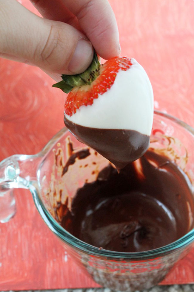 Woman\'s hand dipping a strawberry into a bowl of melted chocolate.
