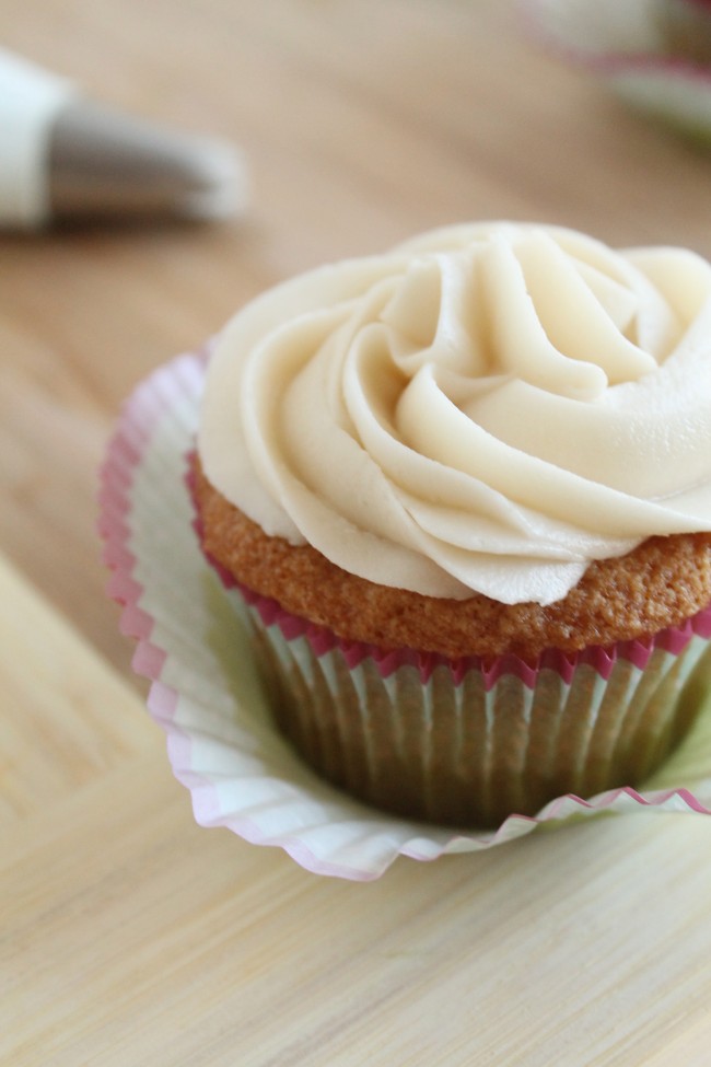 Vanilla cupcake with white frosting sitting in a peeled-off cupcake liner.
