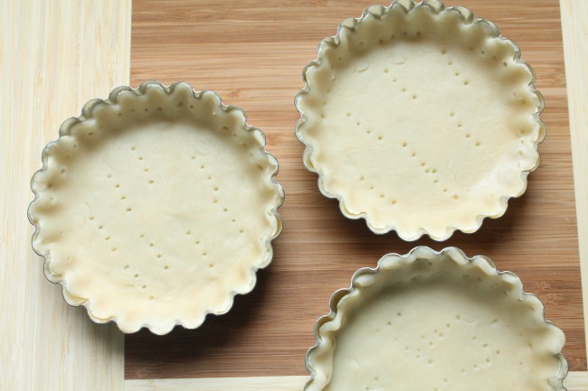 Small tart tins lined with pie dough that has been pierced with a fork.