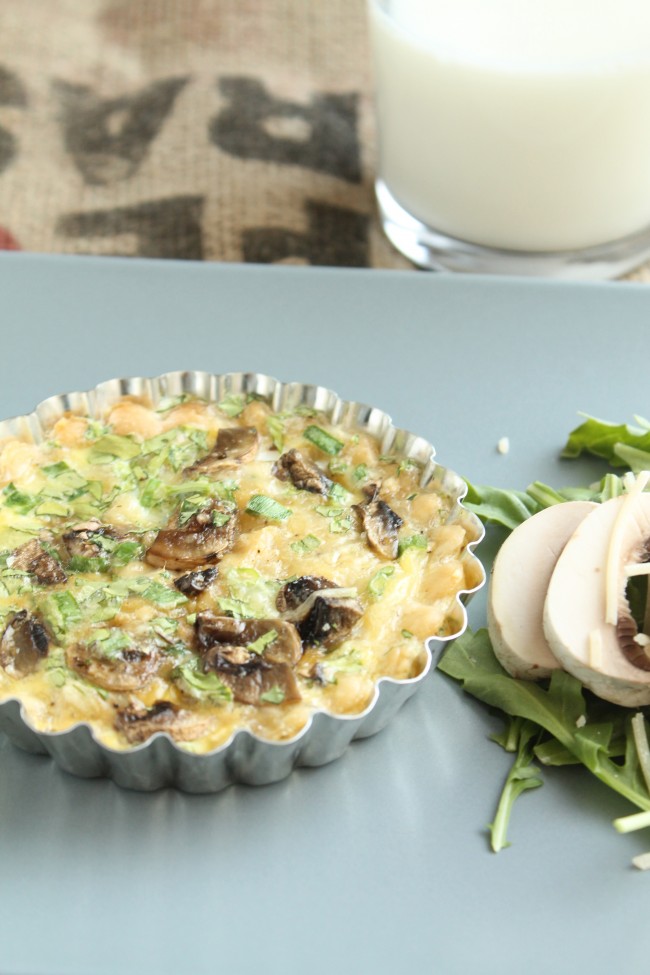 Small metal tin holding a mushroom quiche on a blue plate.