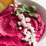 Pink beet dip in a white bowl topped with fresh basil.