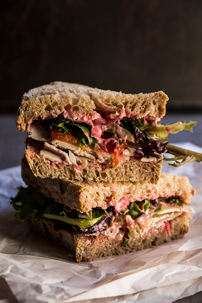 Two sandwich halves stacked on top of each other, showing layers of turkey, cranberry mayonnaise, greens, and tomatoes.