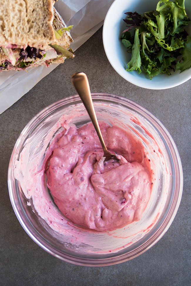 Cranberry mayonnaise in a glass bowl next to a bowl of fresh greens and a turkey sandwich.