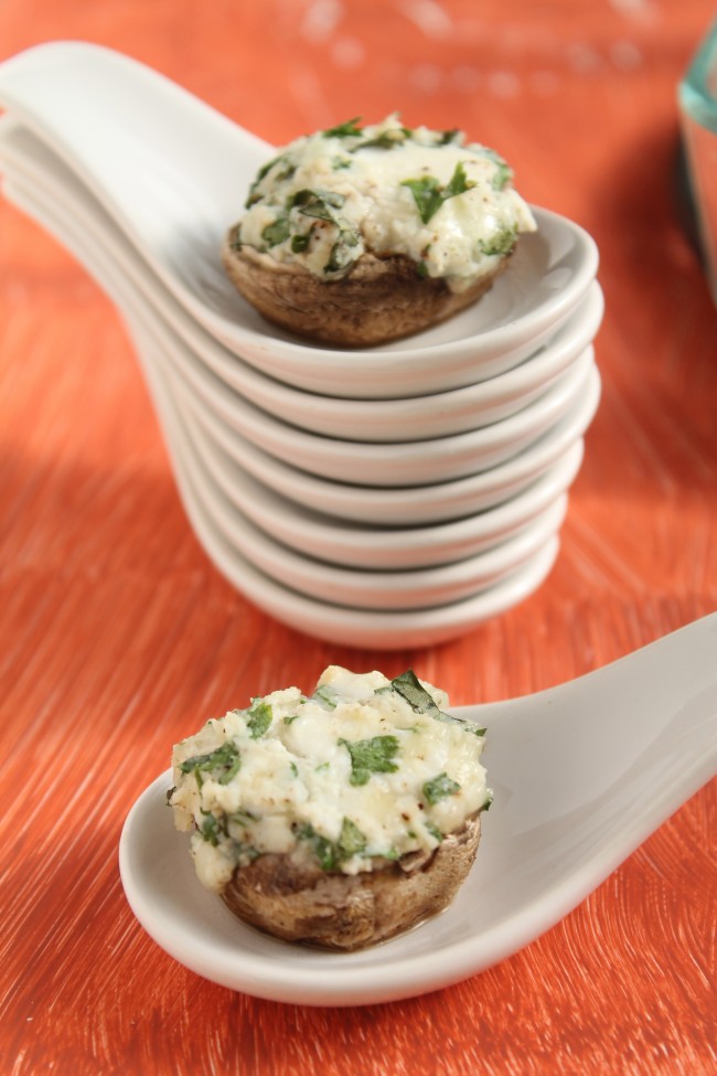 A stack of white ceramic appetizer spoons with a cheese stuffed mushroom on top.
