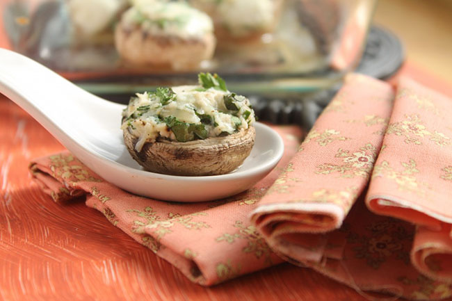 Cheese and herb stuffed mushroom sitting on a large white appetizer spoon next to an orange napkin.
