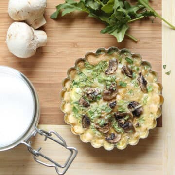 Mushroom quiche in a small tart pan, sitting on a wooden surface.