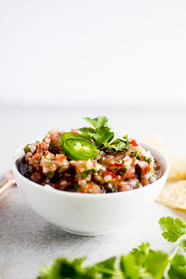 White bowl filled with fresh salsa in front of a white background.
