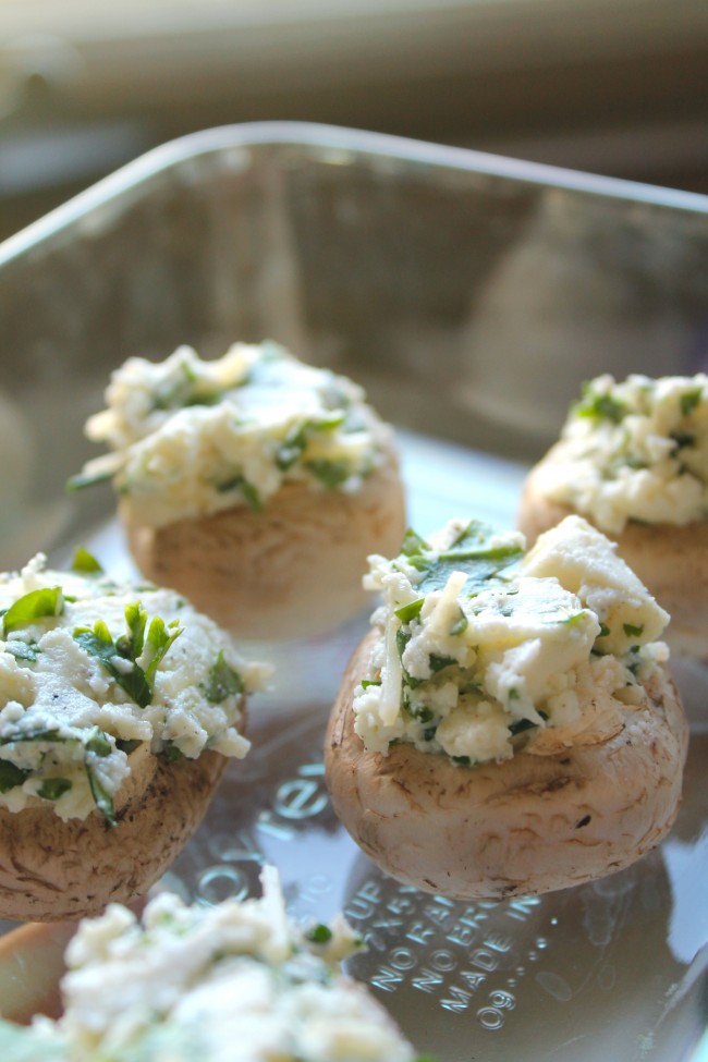 Baby portobello mushrooms stuffed with an herb and cheese mixture sitting in a glass baking dish.