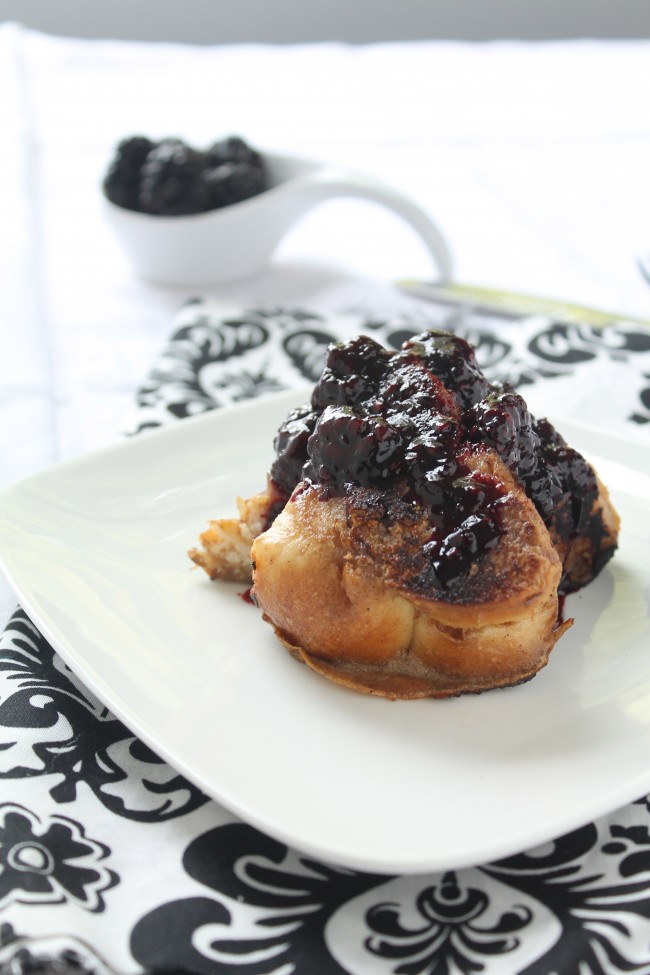 Slices of french toast topped with blackberry syrup, sitting on a white serving plate.