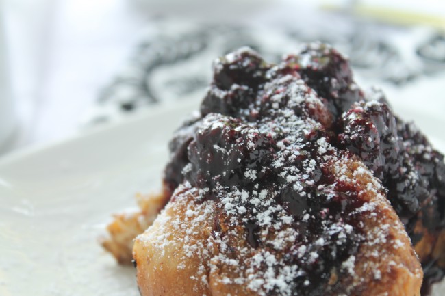 Close up of a piece of french toast topped with blackberries and powdered sugar.