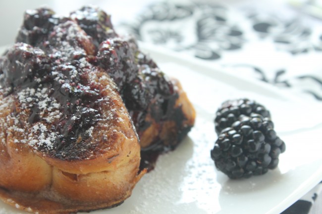 Slices of french toast on a white plate next to fresh blackberries.