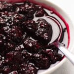 Blackberry sauce in a white bowl with a spoon.