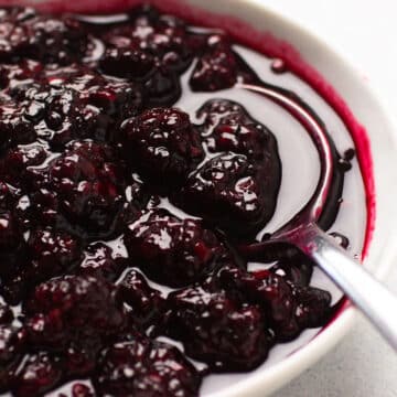 Blackberry sauce in a white bowl with a spoon.