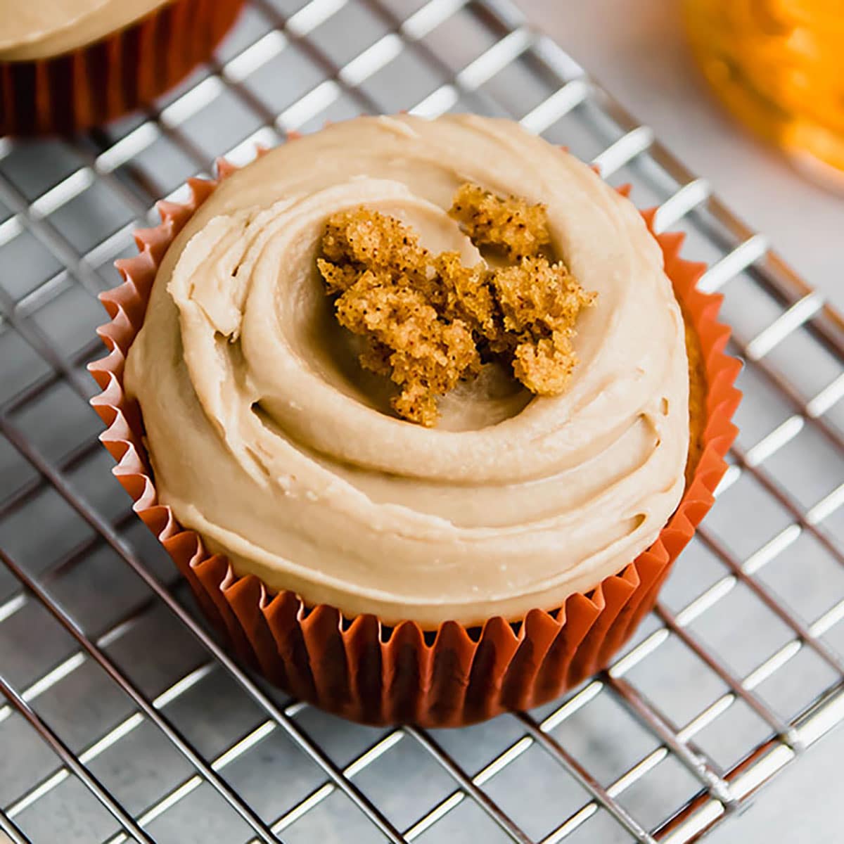 Pumpkin cupcake with maple frosting sitting on a wire cooling rack.