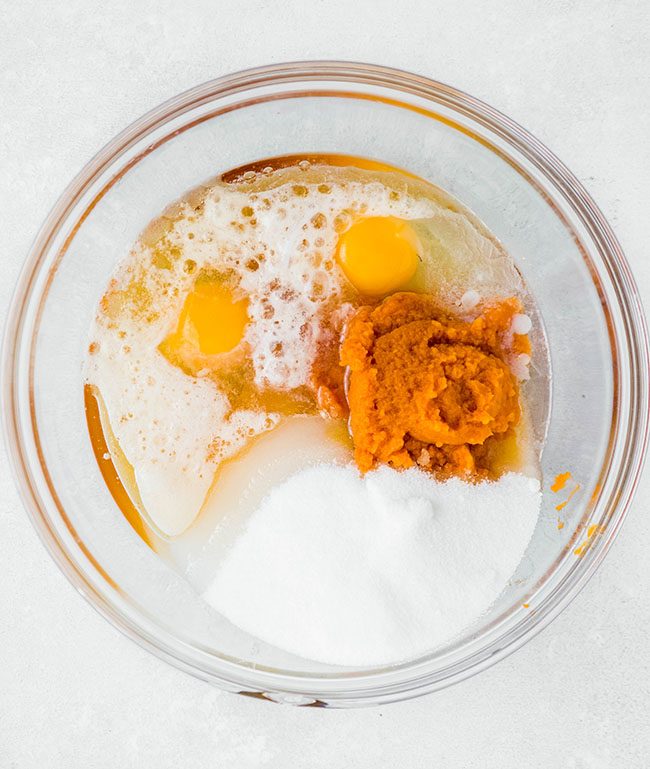 Eggs, pumpkin purée, and sugar in a glass mixing bowl.