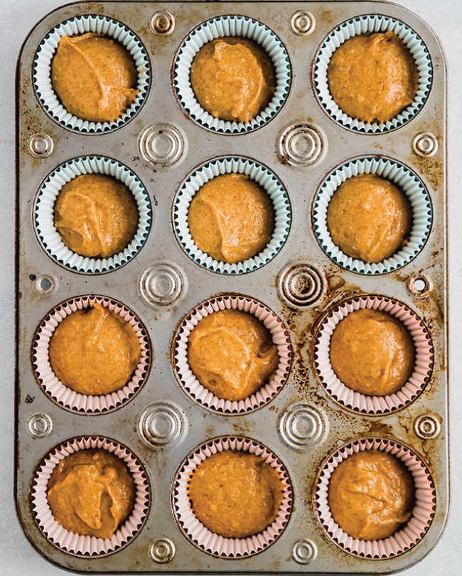 A cupcake tin full of orange batter waiting to be baked.
