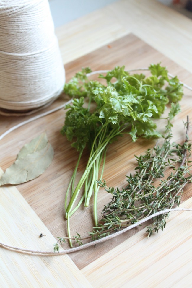 Fresh herbs on a wooden cutting board next to a roll of kitchen twine.