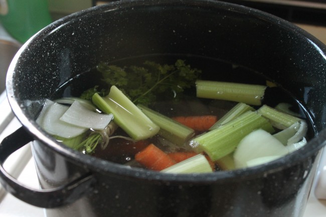 Celery, carrots, onions, and herbs in a large black pot filled with water.