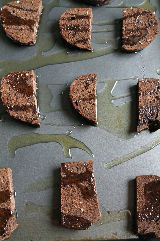 Pumpernickel slices drizzled with olive oil on a sheet pan.