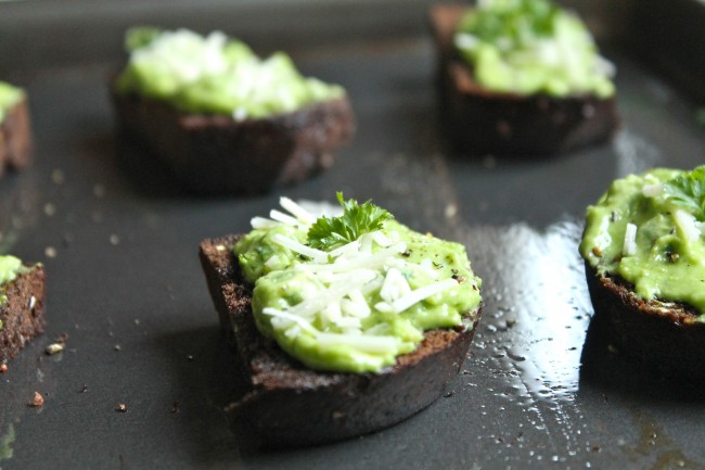 Pumpernickel toast topped with green pea dip, sitting on a dark serving platter.