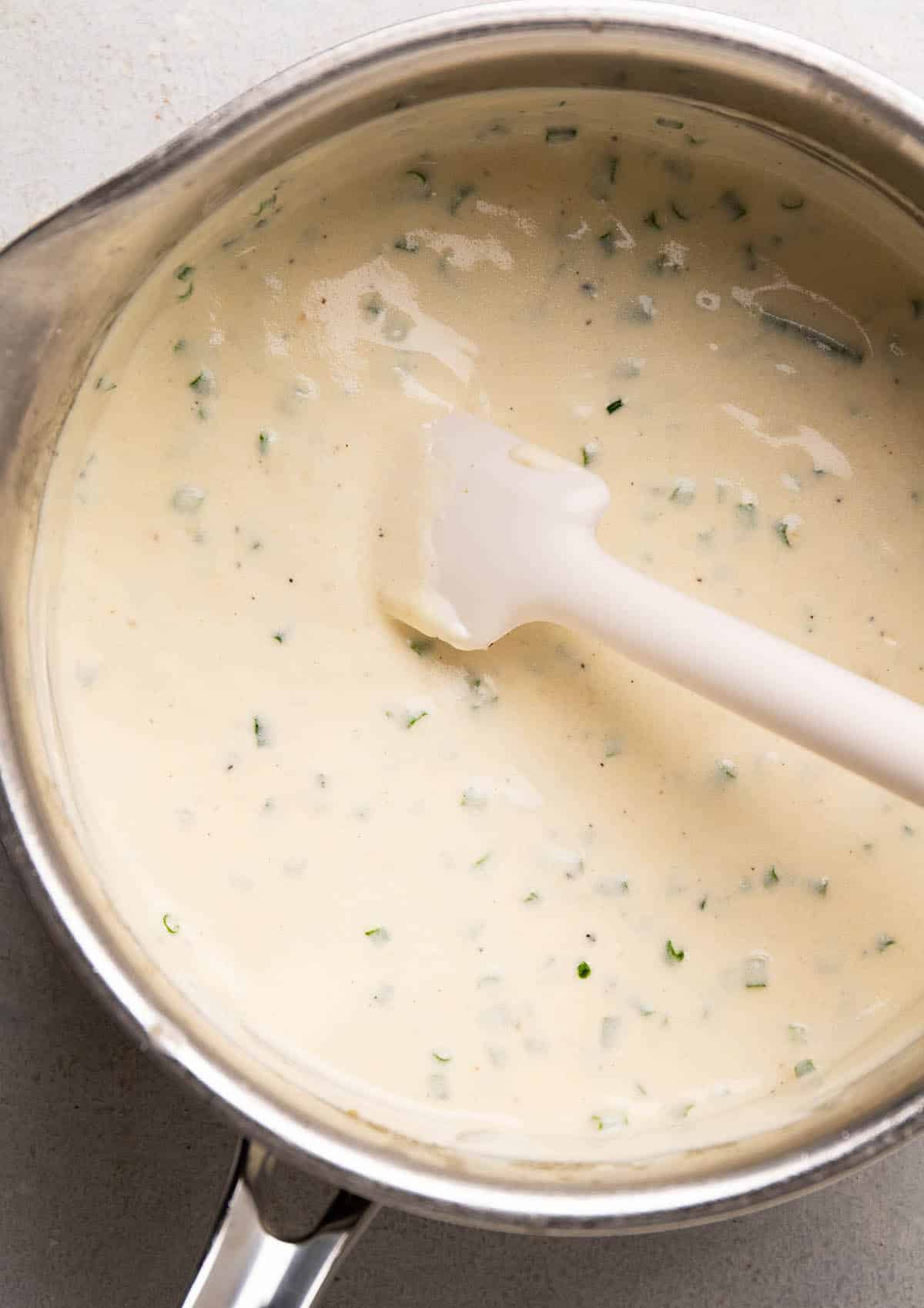 White spatula stirring sour cream and chives into sauce.