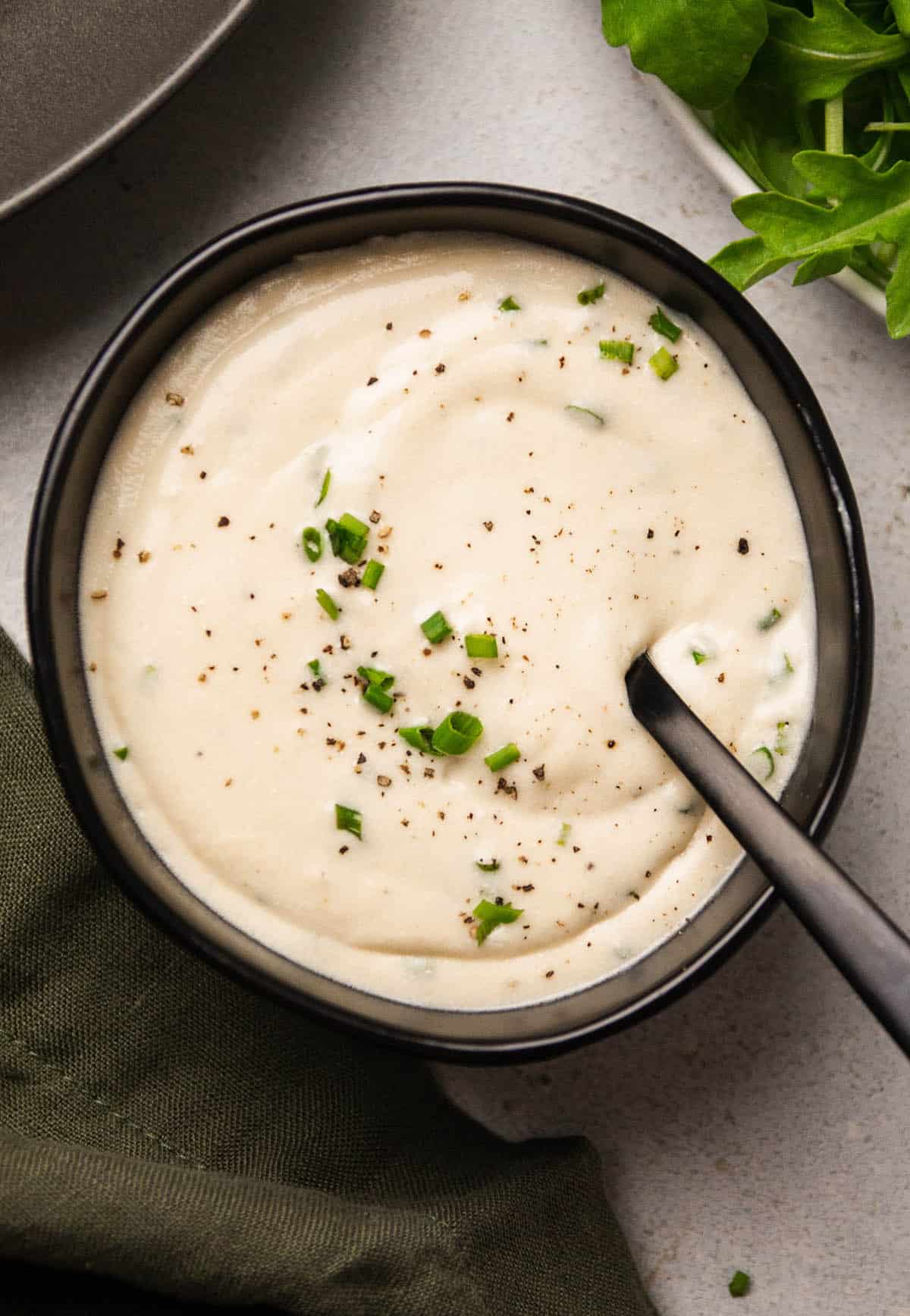 Sour cream sauce topped with fresh chives in a black bowl.