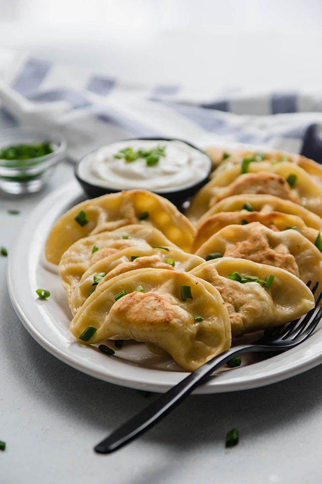 Pierogi garnished with chopped chives on a white plate with a black serving fork.