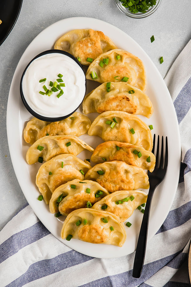 Pierogi topped with chives on a white plate next to a blue napkin.