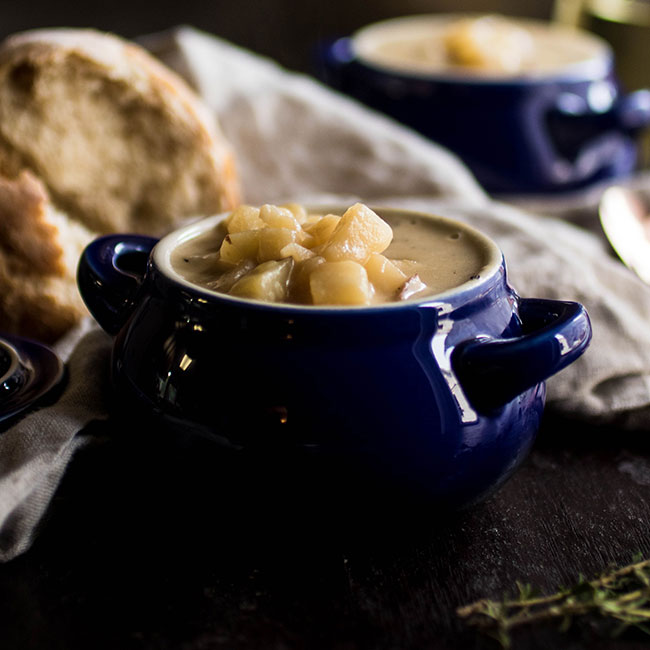 Two small blue bowls filled with potato soup, next to a hunk of crusty bread.