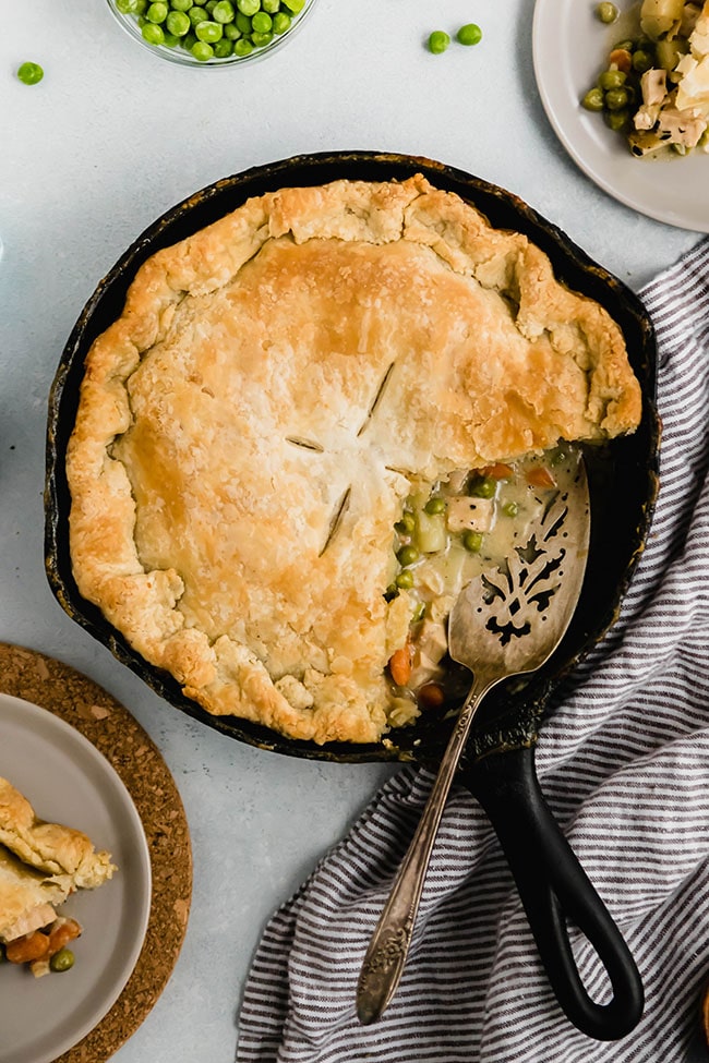 Chicken pot pie in a cast iron skillet with a silver serving knife next to a striped linen napkin.