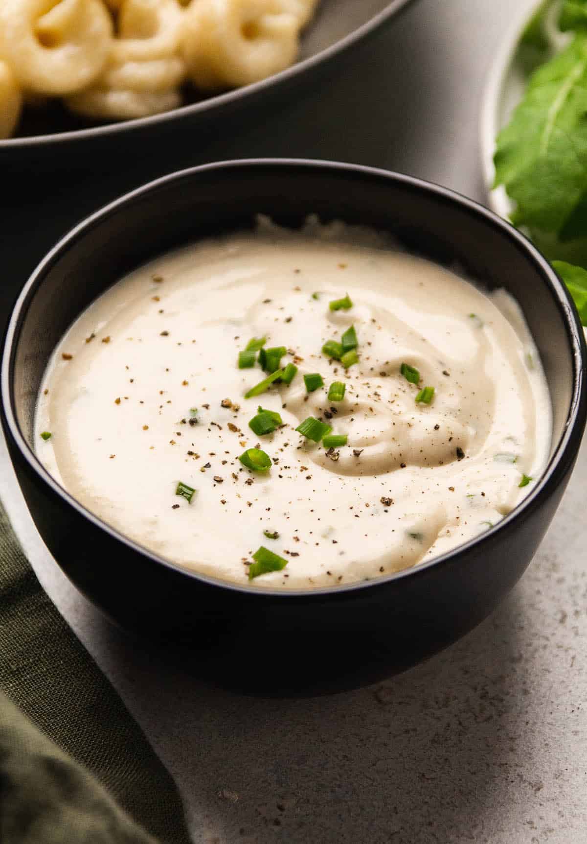 Sour cream sauce in a black bowl, topped with black pepper and fresh chives.