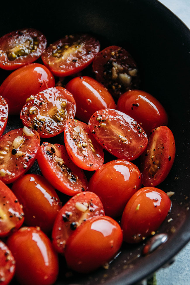 Halved cherry tomatoes in a skillet with garlic.