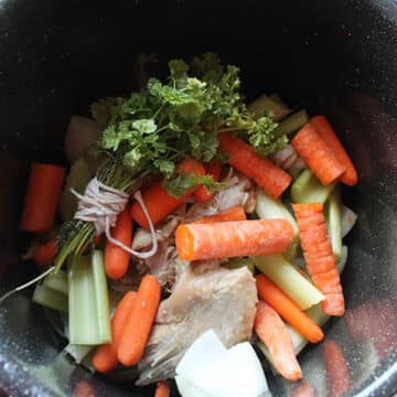 A large black pot filled with turkey, carrots, celery, and herbs.