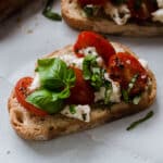 Bruschetta topped with fresh basil, sitting on a white table.