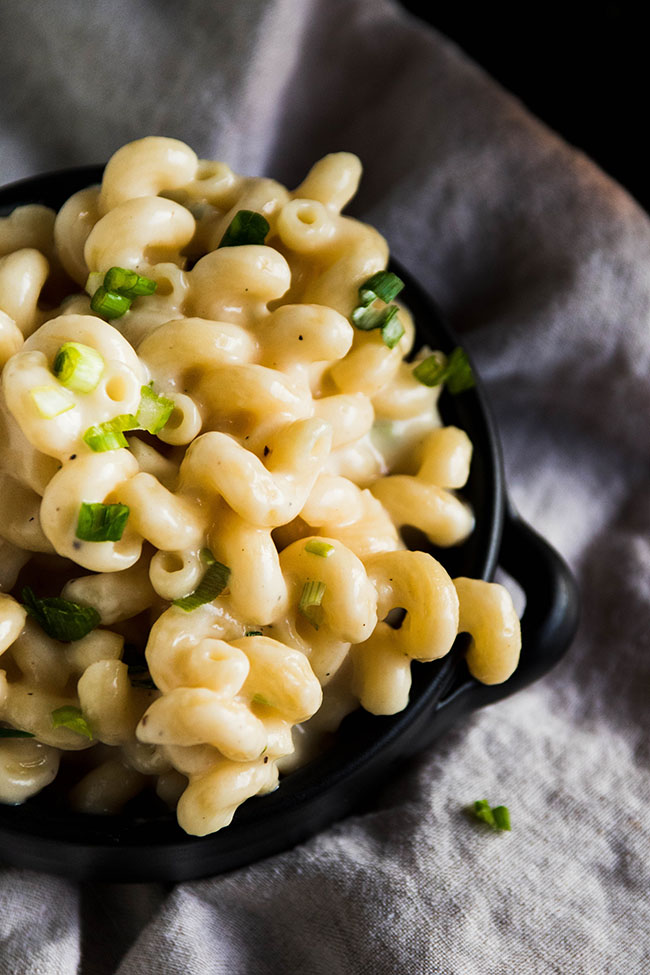 Macaroni and cheese in a small black bowl, garnished with sliced green onions.