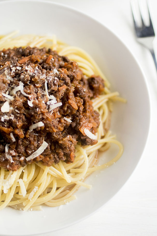 Close up of a bowl of spaghetti noodles topped with dark bolognese sauce and shredded parmesan.