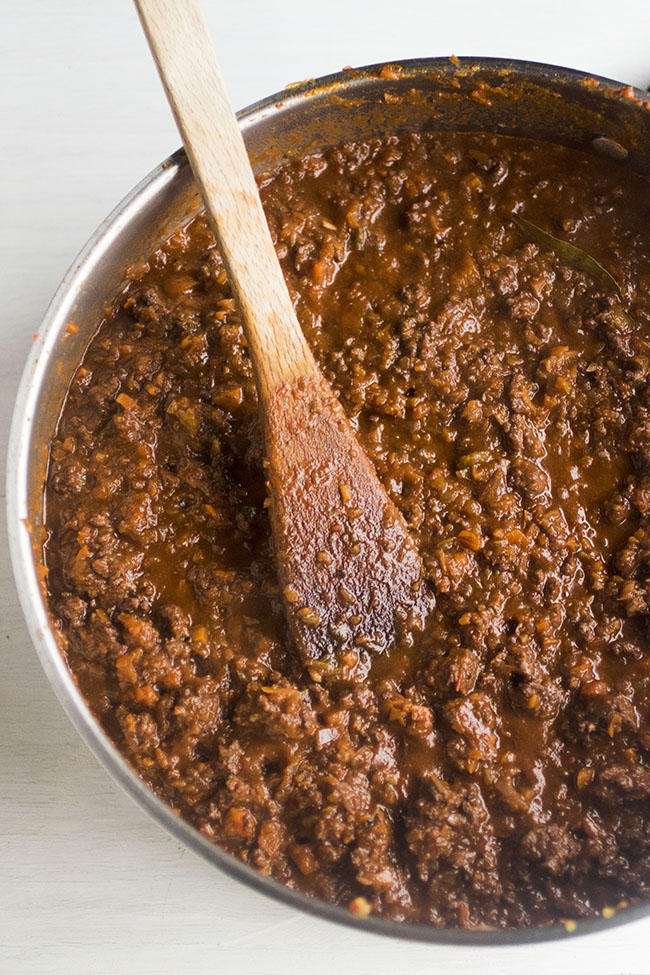 Wooden spoon stirring sausage bolognese in a large skillet.