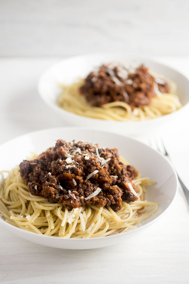 Two white bowls filled with cooked spaghetti and topped with bolognese sauce.